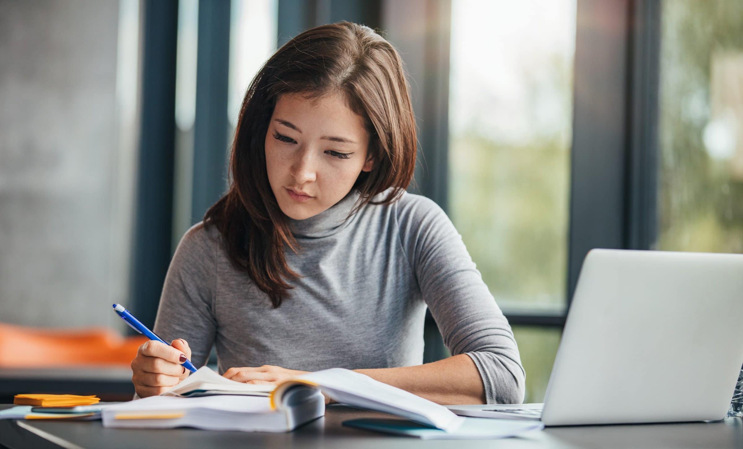 Shot of young woman taking down notes in diary. Female university student preparing note for the exam at library.