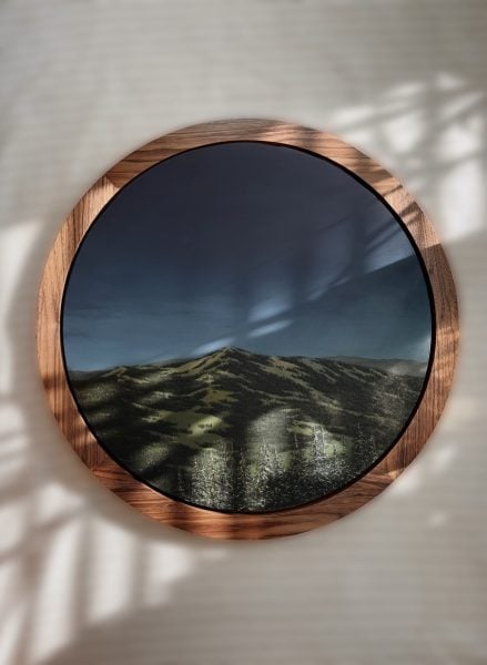 Wooden circular frame with painting of a dark blue sky and green mountains in the foreground