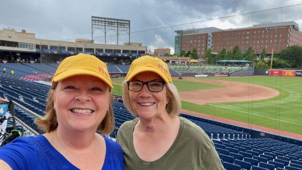 Two P.E.O.s in the stands at a baseball park wearing yellow P.E.O. ball caps
