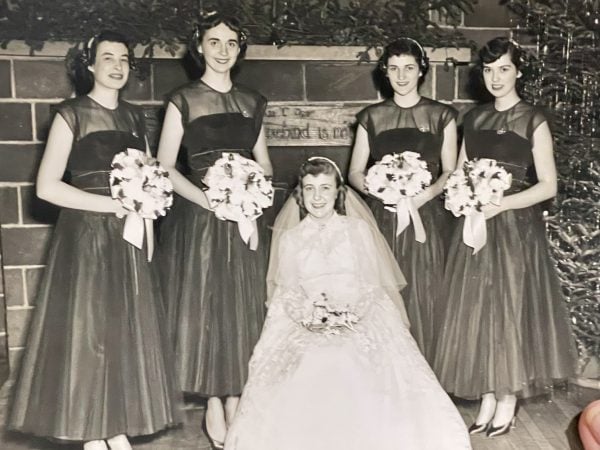 Black and white wedding photo from the 1950s. Bride is seated with four bridesmaids standing behind her. 