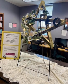 A wooden star on an easel with the letters P.E.O. on it. A small sign has information about P.E.O. and its involvement in the history of the library 