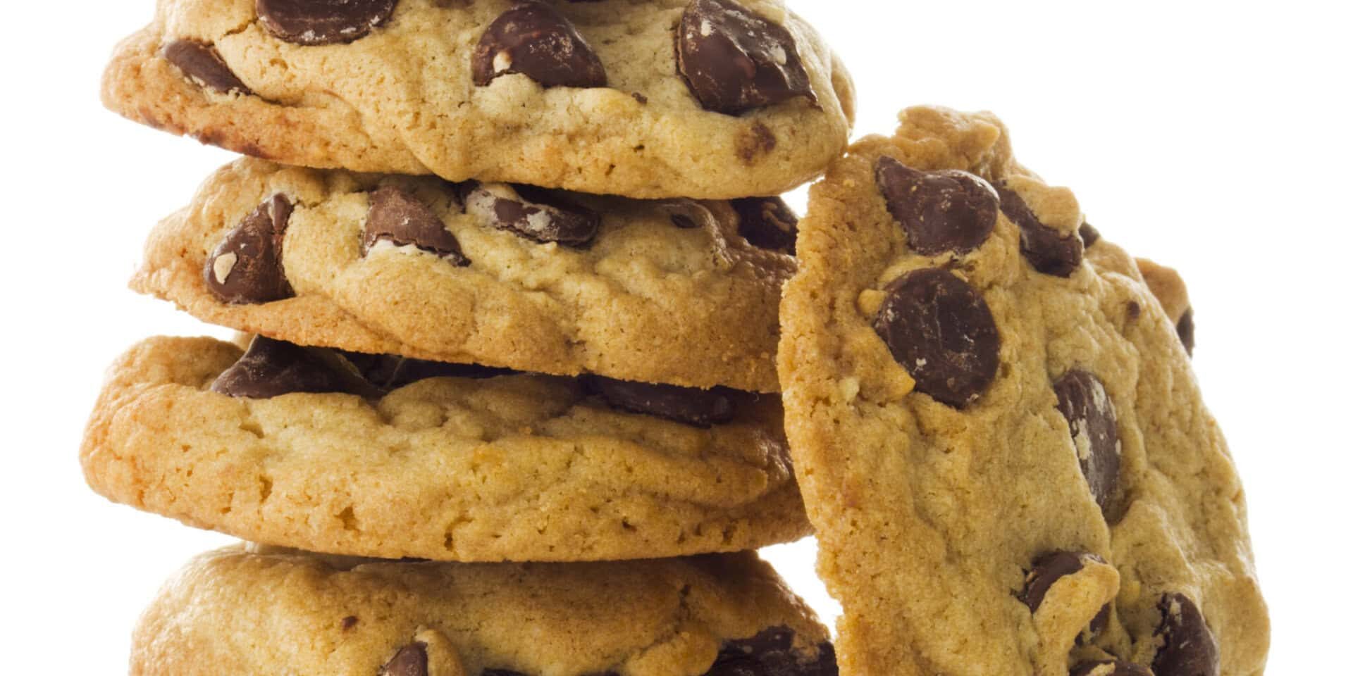 Fresh, homemade chocolate chip cookies stacked in vertical tower of six morsels. One piece leans against the pile. The baked, gourmet dark chocolate treat is a favorite dessert or after-school snack with milk. The sweet food indulgence contributes to overeating fats and sugars, an unhealthy diet. Isolated on white background.