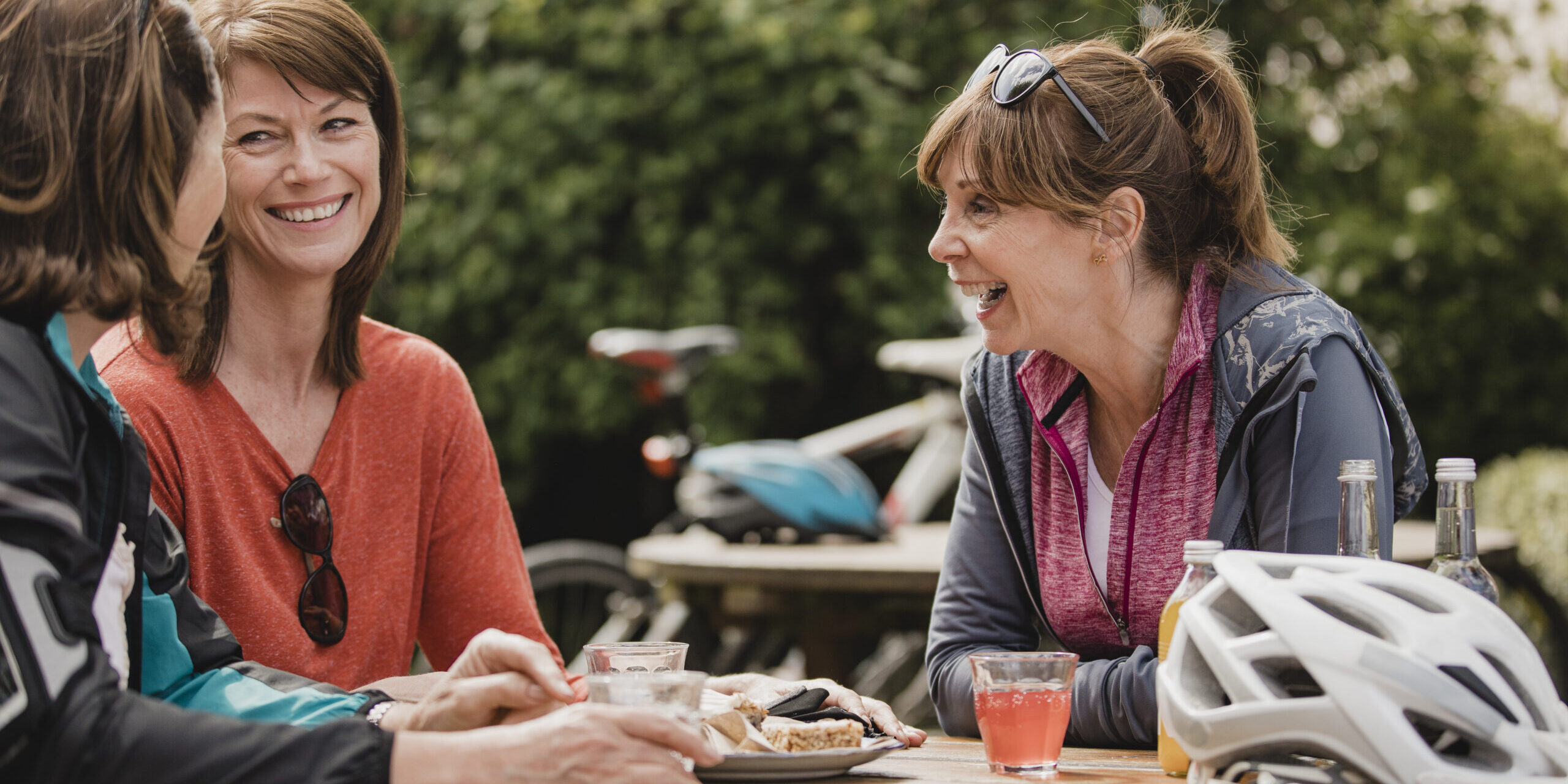 Small group of mature female cyclists sitting down in the outside seating area of a cafe. Tey are enjoying some refreshments as they take a break
