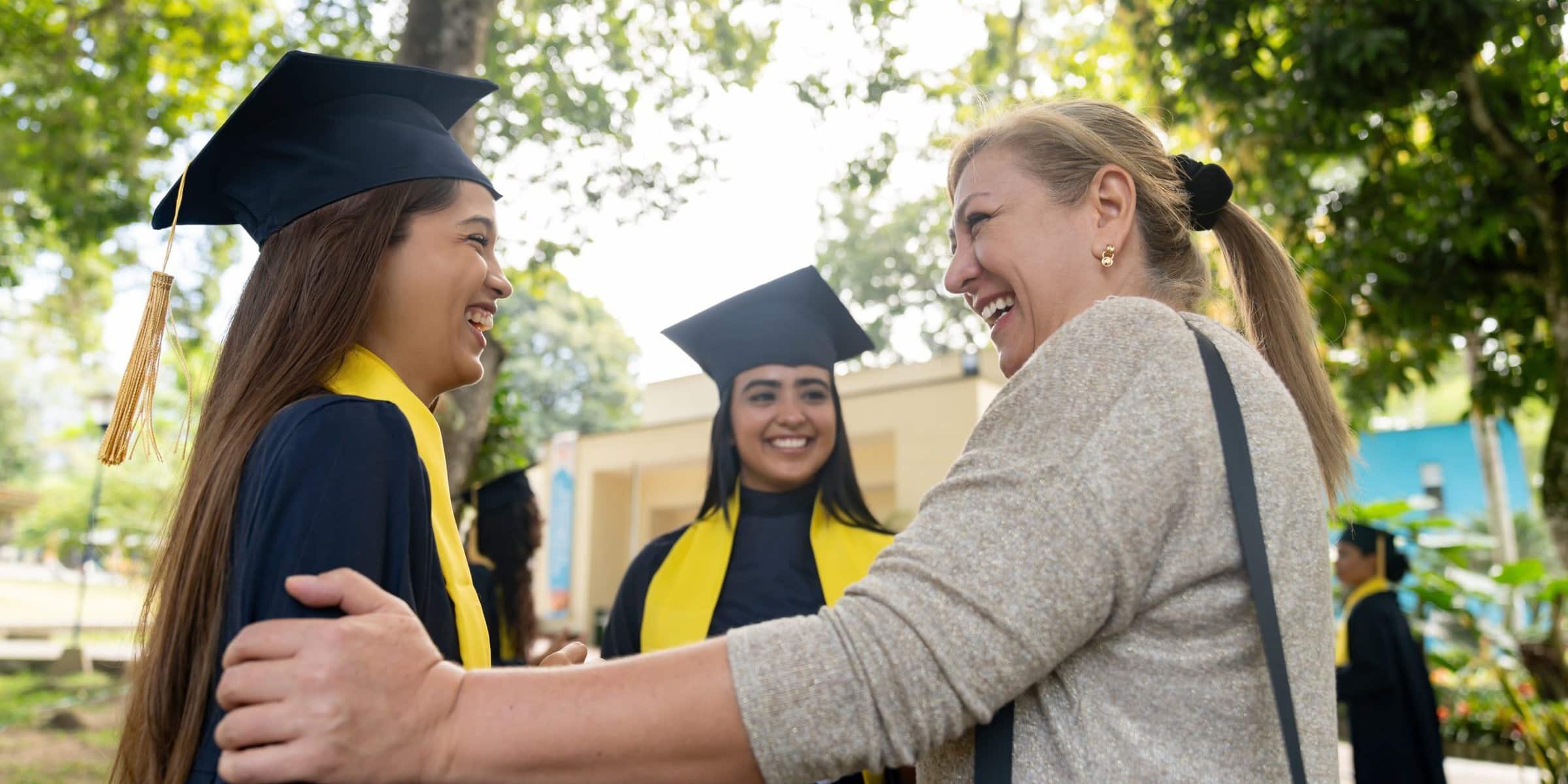 Happy mother talking to her daughter and friends on their graduation day and smiling - education concepts