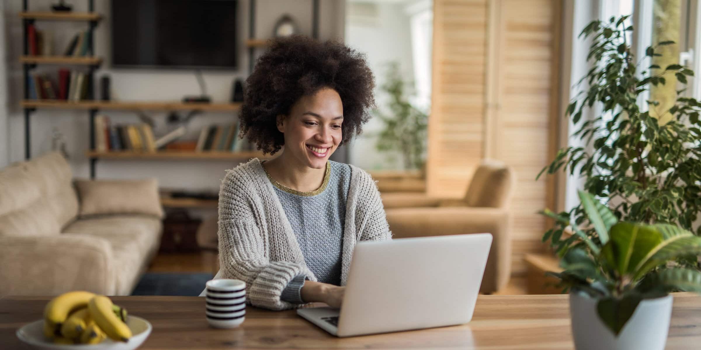 Young happy African American woman using laptop and surfing the net at home.