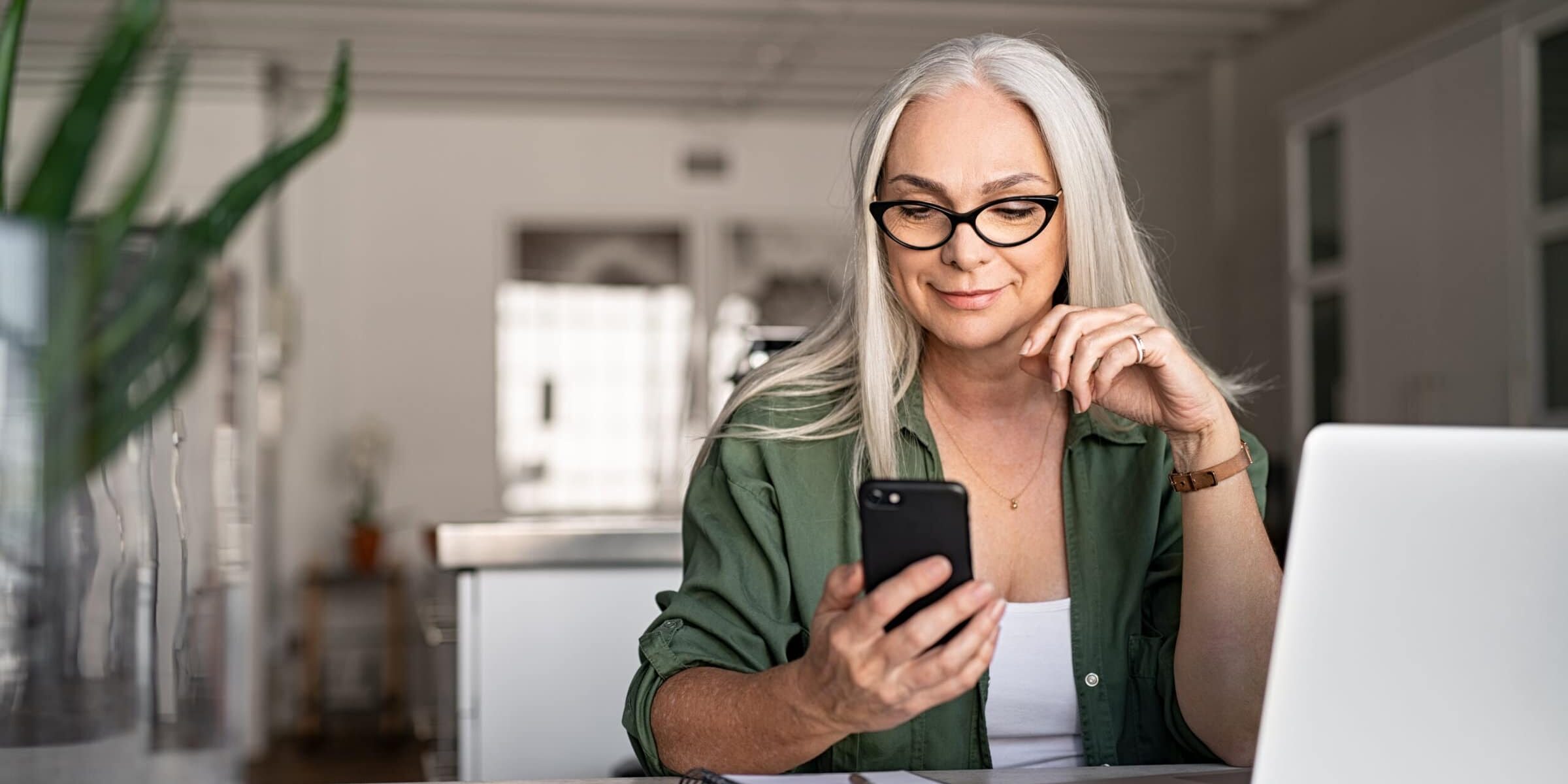 Woman using her phone and computer in the kitchen